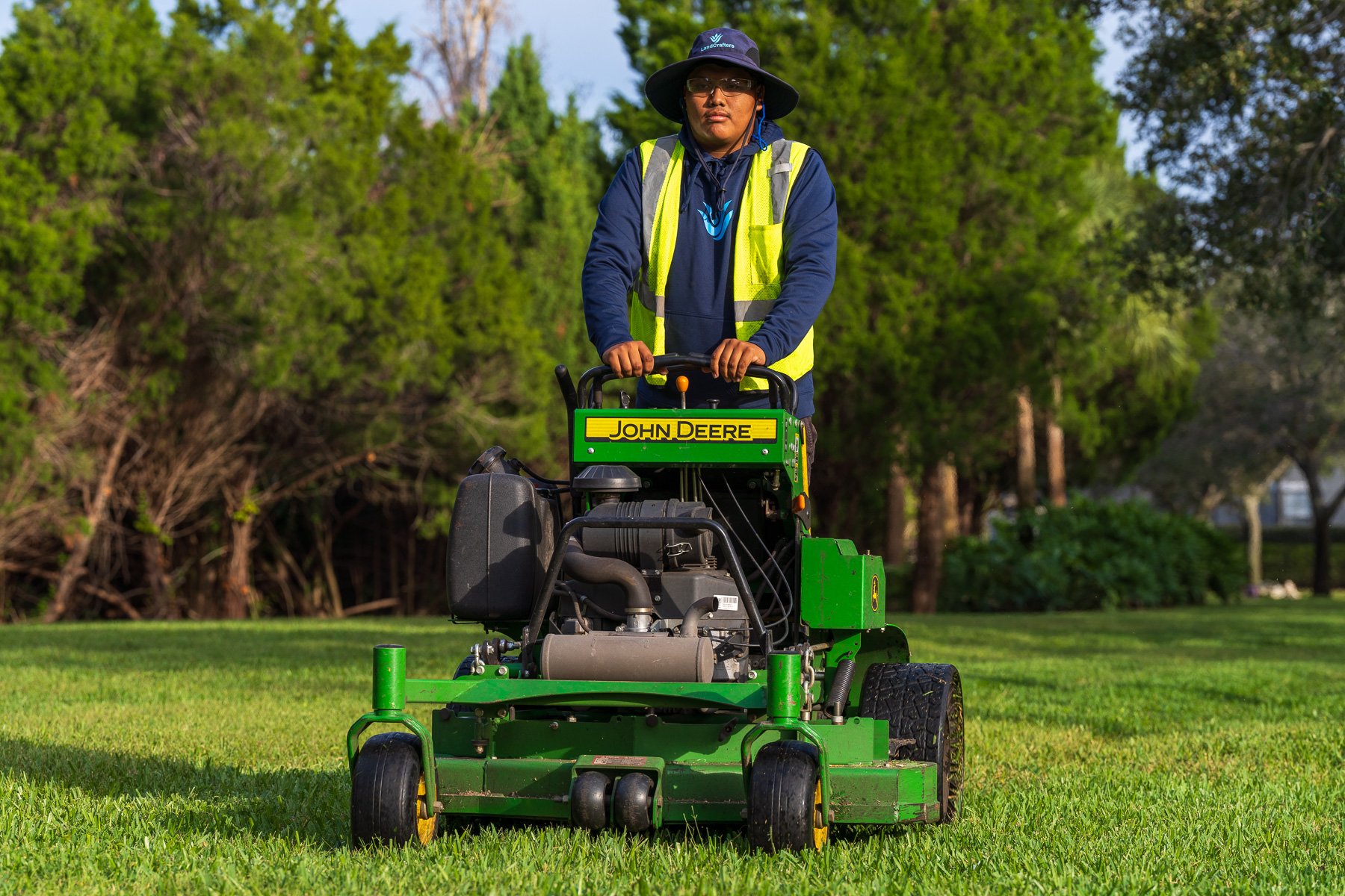 landscape crew member mowing large green grass area 